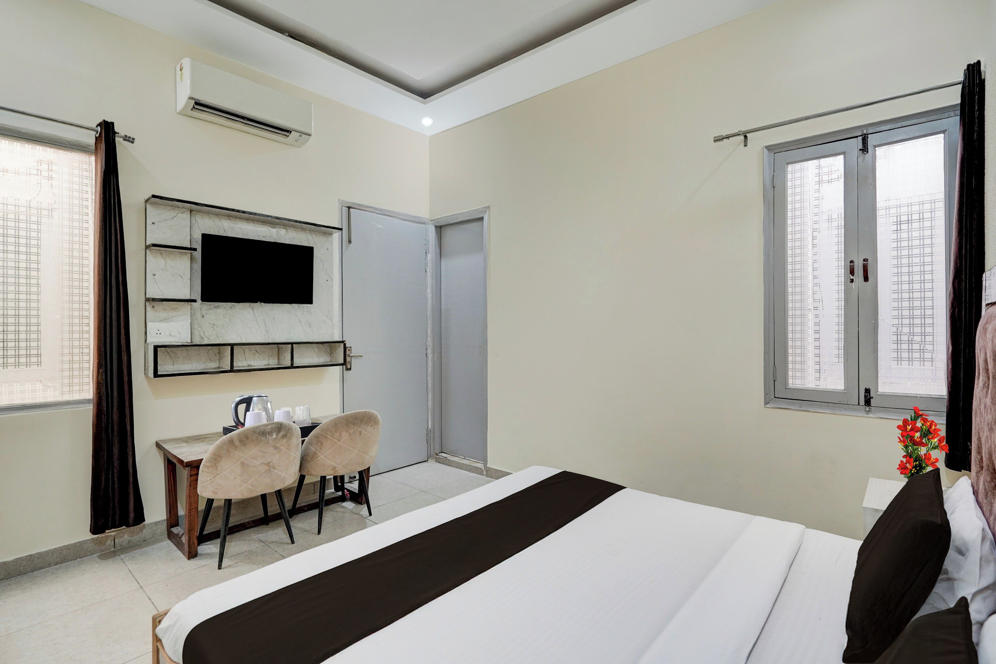 Een hotelkamer met een bed, een bureau met stoelen, een televisie en een raam met gordijnen.