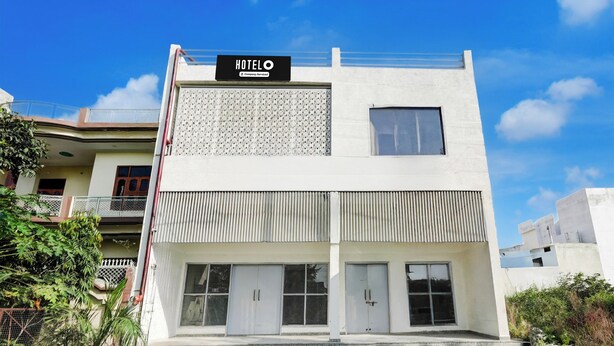 A modern hotel with a sign reading 'HOTELO' and a company-serviced symbol. It features a flat roof, large windows, and a gated entrance.