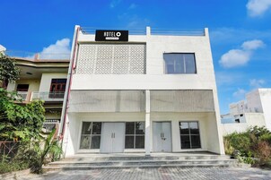 A modern hotel with a sign reading 'HOTELO' and a company-serviced symbol. It features a flat roof, large windows, and a gated entrance.