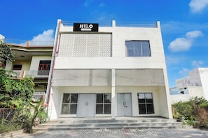 A modern hotel with a sign reading 'HOTELO' and a company-serviced symbol. It features a flat roof, large windows, and a gated entrance.