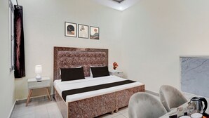 A hotel room with a bed, a nightstand, a desk with a chair, a window, and artwork on the wall.