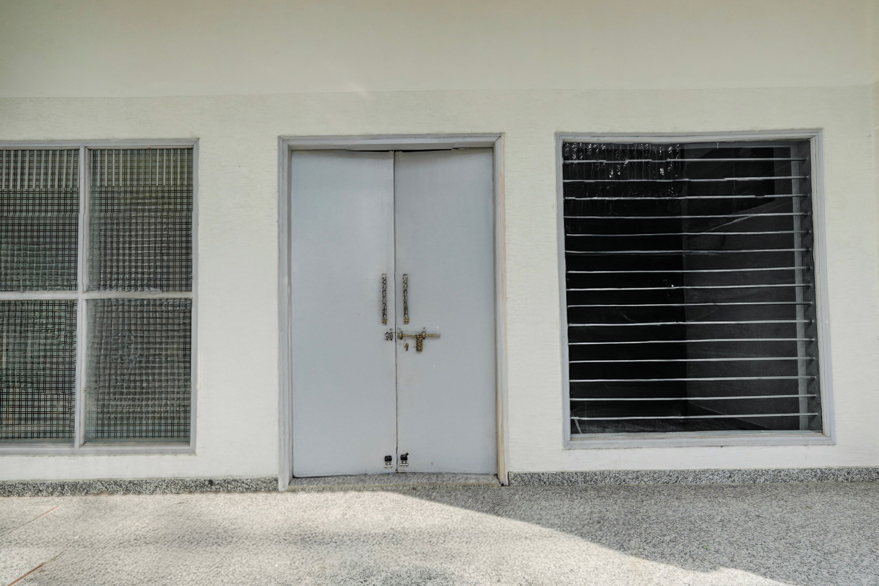 Una puerta blanca con un cerrojo de cadena, una ventana con barrotes de metal y suelo de concreto.