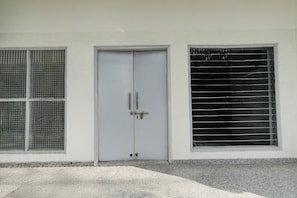 Una puerta blanca con un cerrojo de cadena, una ventana con barrotes de metal y suelo de concreto.