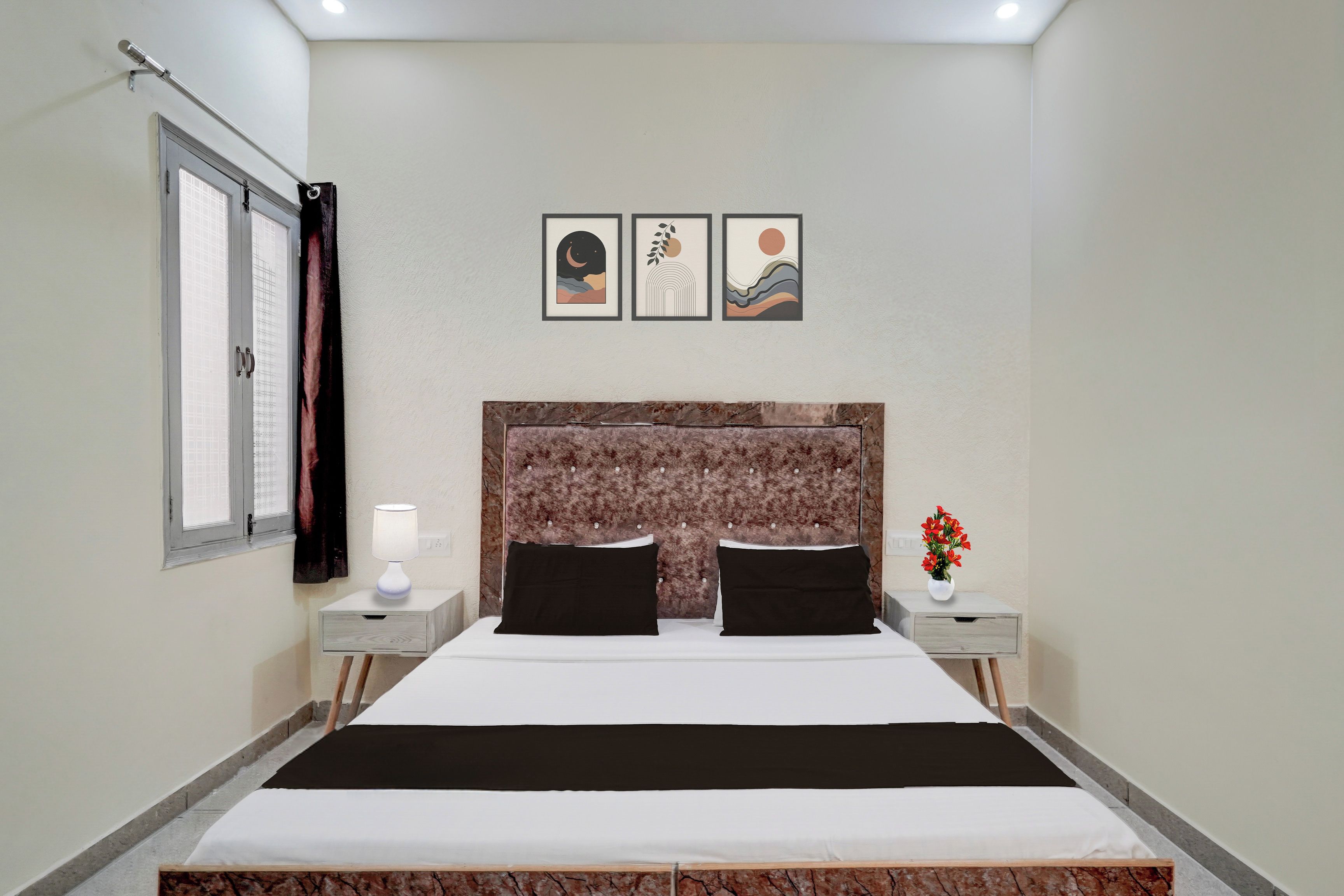 Una habitación de hotel con una cama, dos mesitas de noche, un ventanal con cortinas y tres cuadros colgados en la pared.
