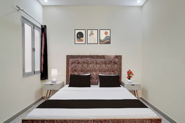 Una habitación de hotel con una cama, dos mesitas de noche, un ventanal con cortinas y tres cuadros colgados en la pared.