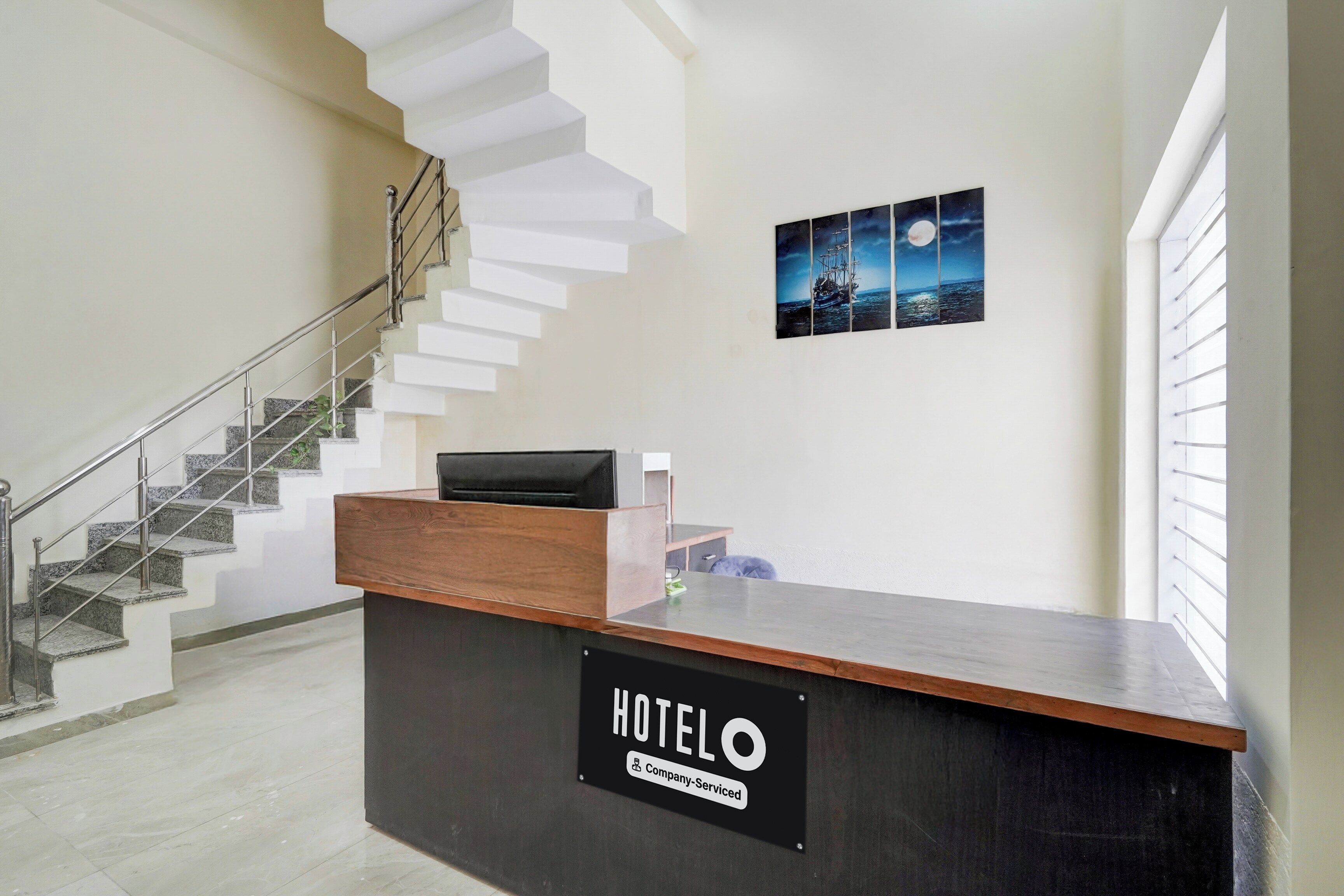 Un mostrador de recepción de hotel con un cartel que indica servicio de empresa. Se ve una escalera con barandilla de metal a la izquierda.