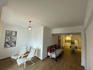 Un soggiorno con divano, due poltrone, un'area pranzo con tavolo e sedie, una cucina sullo sfondo e una lampada a sospensione.