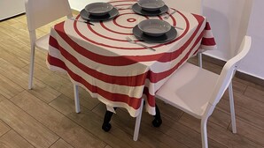 Une table à manger recouverte d’une nappe à rayures, avec quatre assiettes et des couverts, entourée de chaises blanches.