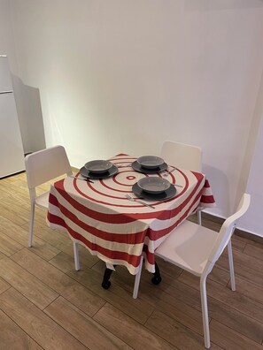 Un tavolo da pranzo con tovaglia a righe, quattro piatti e posate, circondato da sedie bianche.