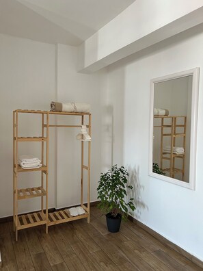 Une pièce avec une étagère en bois où sont pliées des serviettes, un pot de plante et un miroir qui reflète l’étagère.