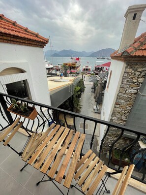 Un balcon doté de meubles en bois, d’un mur en pierre et offrant une vue sur les bateaux et les montagnes.