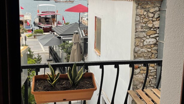 Un balcon donnant sur une marina, un mur en pierre et un parasol rouge.