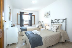 Ein Hotelzimmer mit zwei Betten, einem Schreibtisch, einem Spiegel, einem Fenster mit Vorhängen und einer Wandlampe.