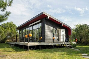 A modern cabin with a glass enclosure, wooden deck, and a red roof. - Architect-designed home with a maritime look (Sjællands Odde)