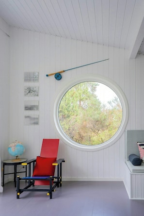 A room with a round window, a red and blue chair, a globe, and wall art. - Architect-designed home with a maritime look (Sjællands Odde)