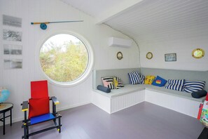 A room with a round window, a red chair, a bench with striped pillows, and wall-mounted artwork. - Architect-designed home with a maritime look (Sjællands Odde)