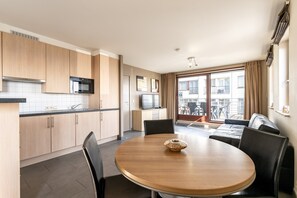 A modern kitchen with wooden cabinets, a microwave, and a dining area with a round table and chairs. - Studio Apartment at Zeedijk With Sea View (Blankenberge)