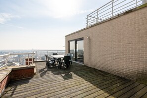 A rooftop terrace with a table and chairs, a brick wall, and a view of the city. - Studio Apartment at Zeedijk With Sea View (Blankenberge)