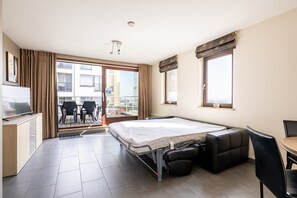 A hotel room with a bed, a desk, a chair, a sofa, a balcony with a view, and a television. - Studio Apartment at Zeedijk With Sea View (Blankenberge)