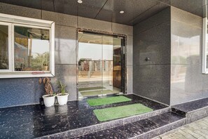 A building entrance with a glass door, potted plants, and a green mat. - Hotel O Sunrakh Road Vrindavan Formerly (Vrindavan)