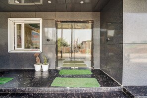 A hotel entrance with a glass door, potted plants, and a small window. - Hotel O Sunrakh Road Vrindavan Formerly (Vrindavan)