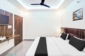 Une chambre à coucher avec un lit, un ventilateur de plafond, un téléviseur fixé au mur et un tableau accroché au mur.