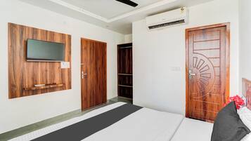 A hotel room with a bed, a flat-screen TV mounted on a wooden panel, a ceiling fan, and a door with a decorative design.