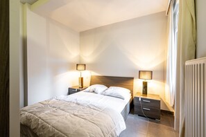 Ein Schlafzimmer mit einem Bett, zwei Nachttischen inklusive Lampen, einem kleinen Tisch und einer Heizung.