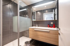 Ein modernes Badezimmer mit Duschkabine aus Glas, einem Holzausleger mit weißem Waschbecken und einem großen Spiegel.