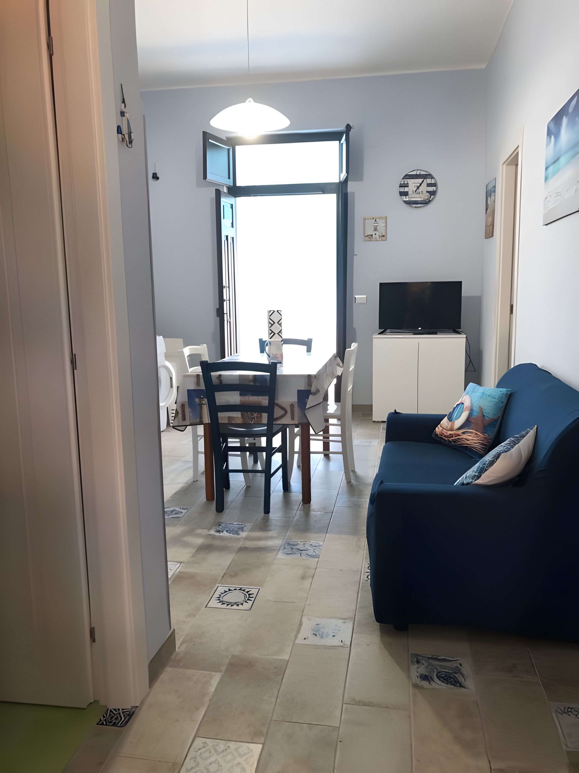 Una sala de estar con un sofá azul, un televisor y un comedor con mesa y sillas.