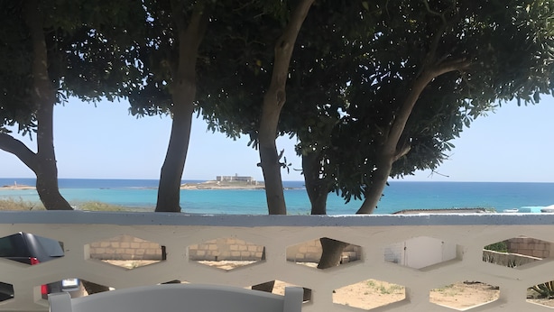 Une terrasse offrant une vue sur la mer, avec une chaise blanche et une table sur laquelle est posée une carte.