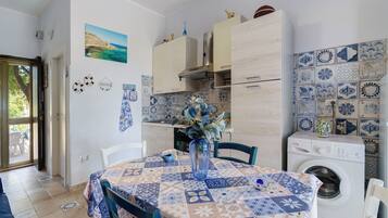 Une cuisine compacte avec un coin repas, comprenant un lave-linge, un pare-feu en carrelage et une vue sur l’extérieur grâce à une porte ouverte.