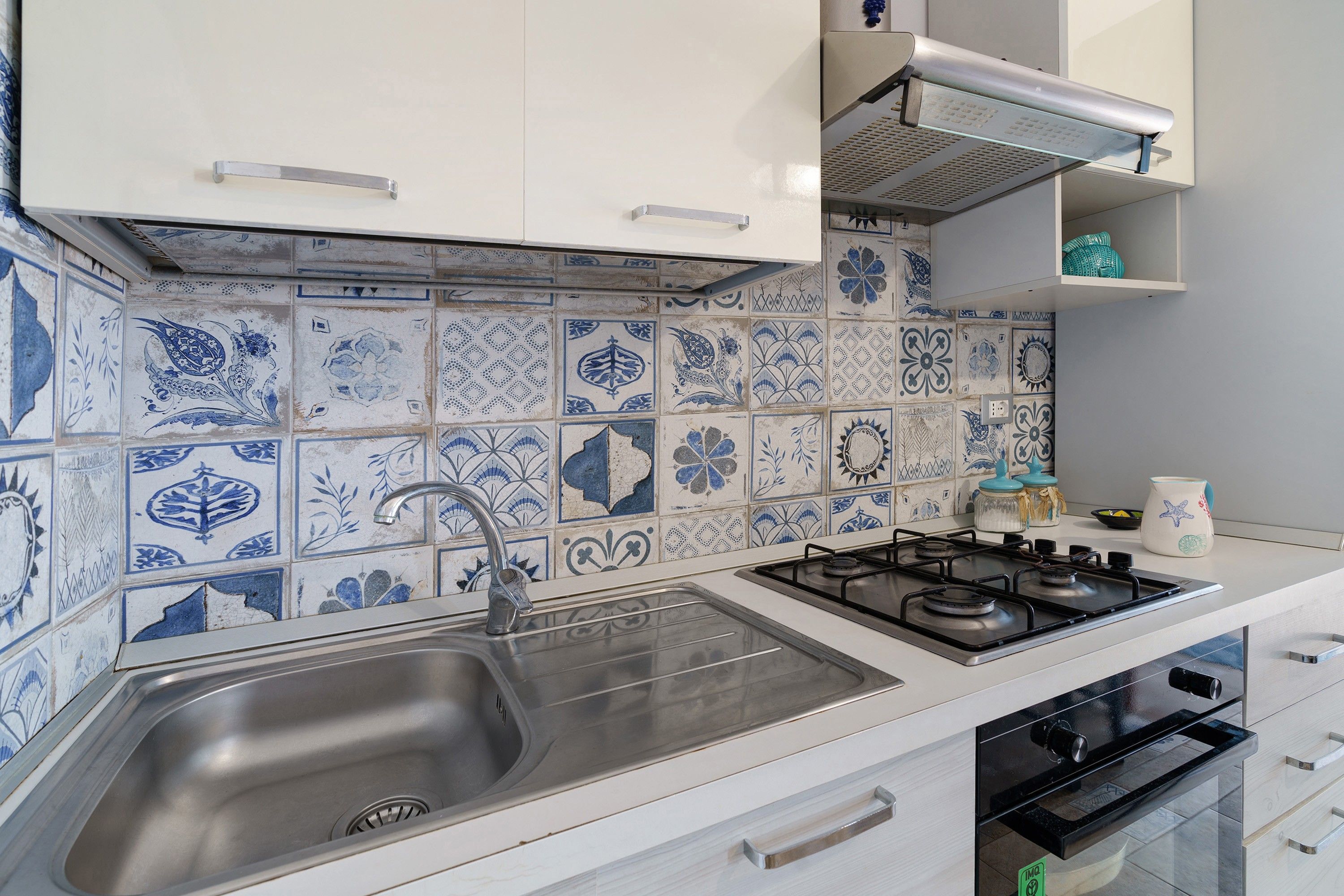 Een keuken met een roestvrijstalen spoelbak, een gasfornuis en een betegelde achterwand.