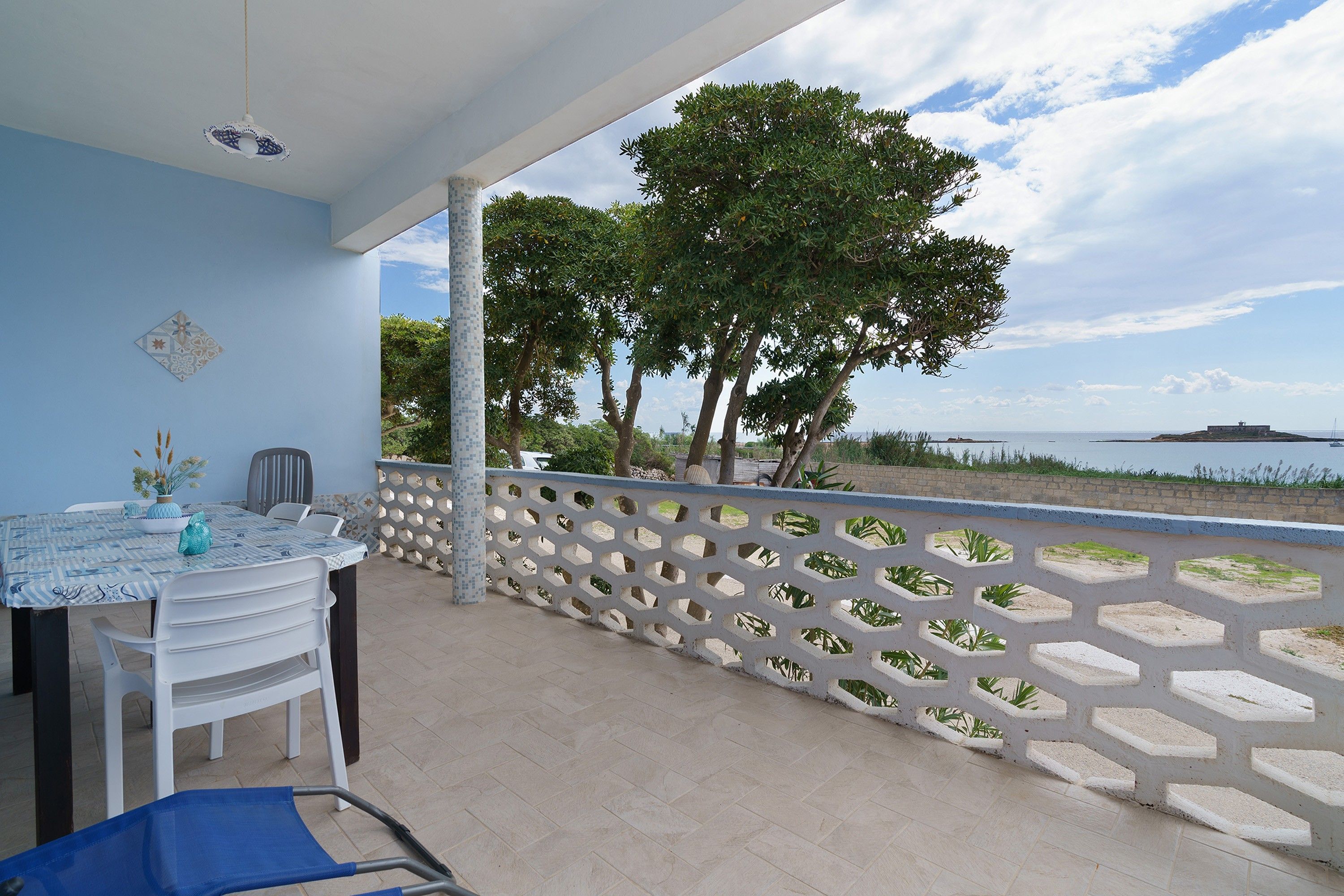 Un balcon avec une table et des chaises, un vase décoratif et une vue sur la mer et les arbres.