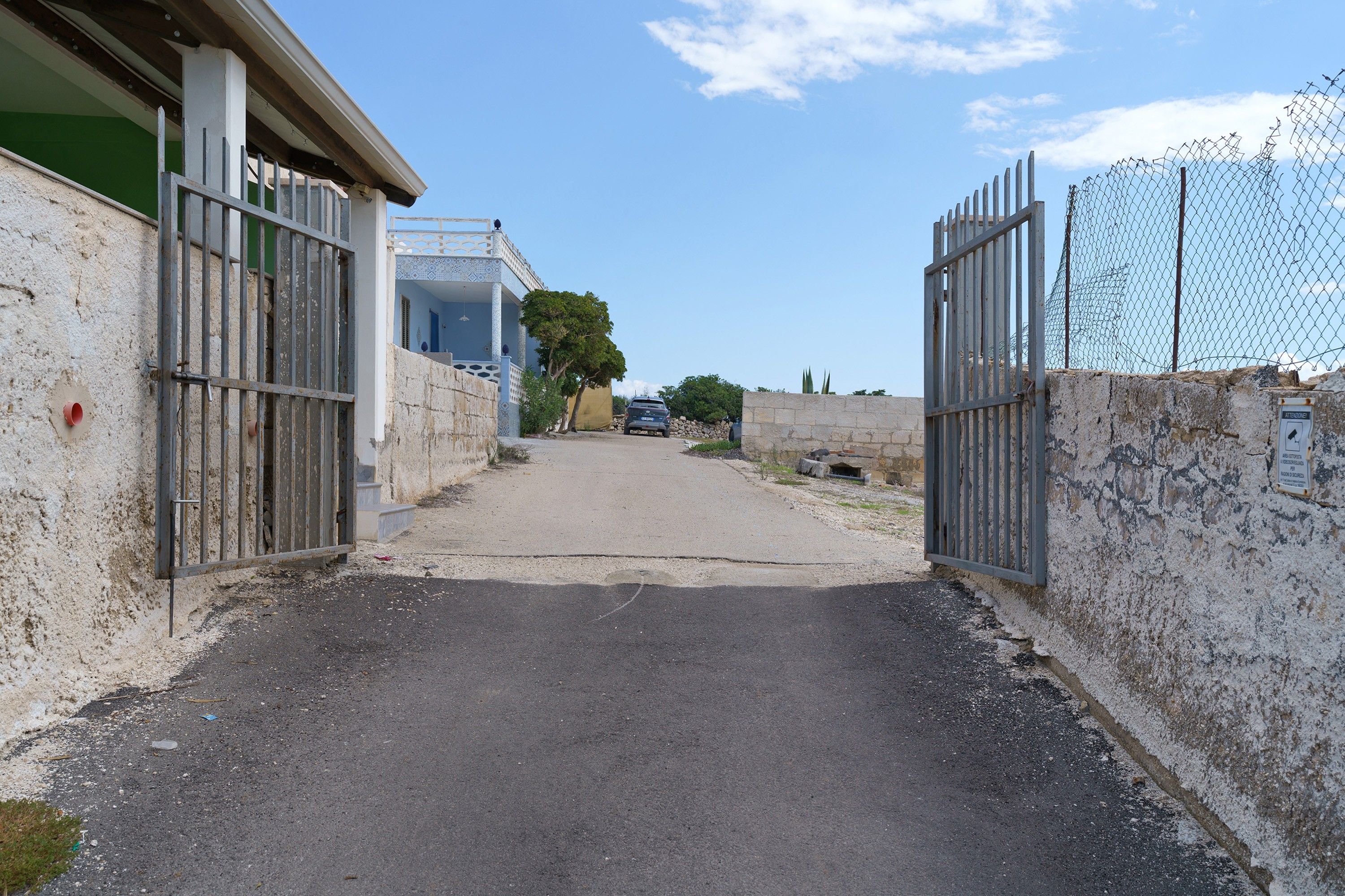A gated entrance to a building with a paved driveway leading to a parked car.