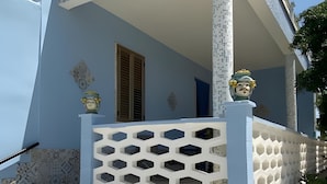 Un bâtiment à la façade bleue, doté d’un balcon blanc orné d’un motif géométrique en treillis et de plantes en pot à l’entrée.