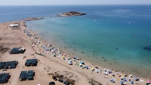 Une plage avec de nombreux parasols et beaucoup de monde, une petite île dans l’eau et un ciel dégagé.