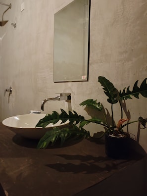 Ein Badezimmer mit einem weißen Waschbecken, einem Spiegel und einer Topfpflanze.