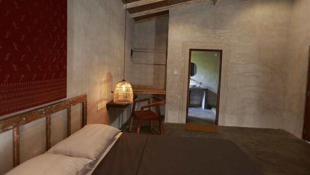 Ein Schlafzimmer mit einem Bett, einem Nachttisch, einem Sessel, einer Hängeleuchte und einer Tür zu einem Badezimmer.