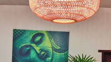 A room with a large Buddha painting, a wooden sofa, a striped chair, a potted plant, and a hanging light fixture.