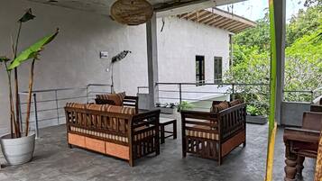 Un espace extérieur aménagé, abrité et doté de deux canapés en bois et d’une table, entouré de plantes en pot et agrémenté d’un luminaire suspendu.