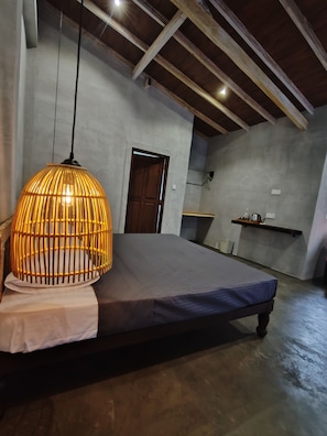 A bedroom with a bed, a hanging light fixture, a wooden door, and a shelf with items.