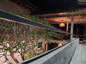 A balcony with a concrete railing, a hanging light fixture, and a view of a building with a brick wall and a wooden ceiling.