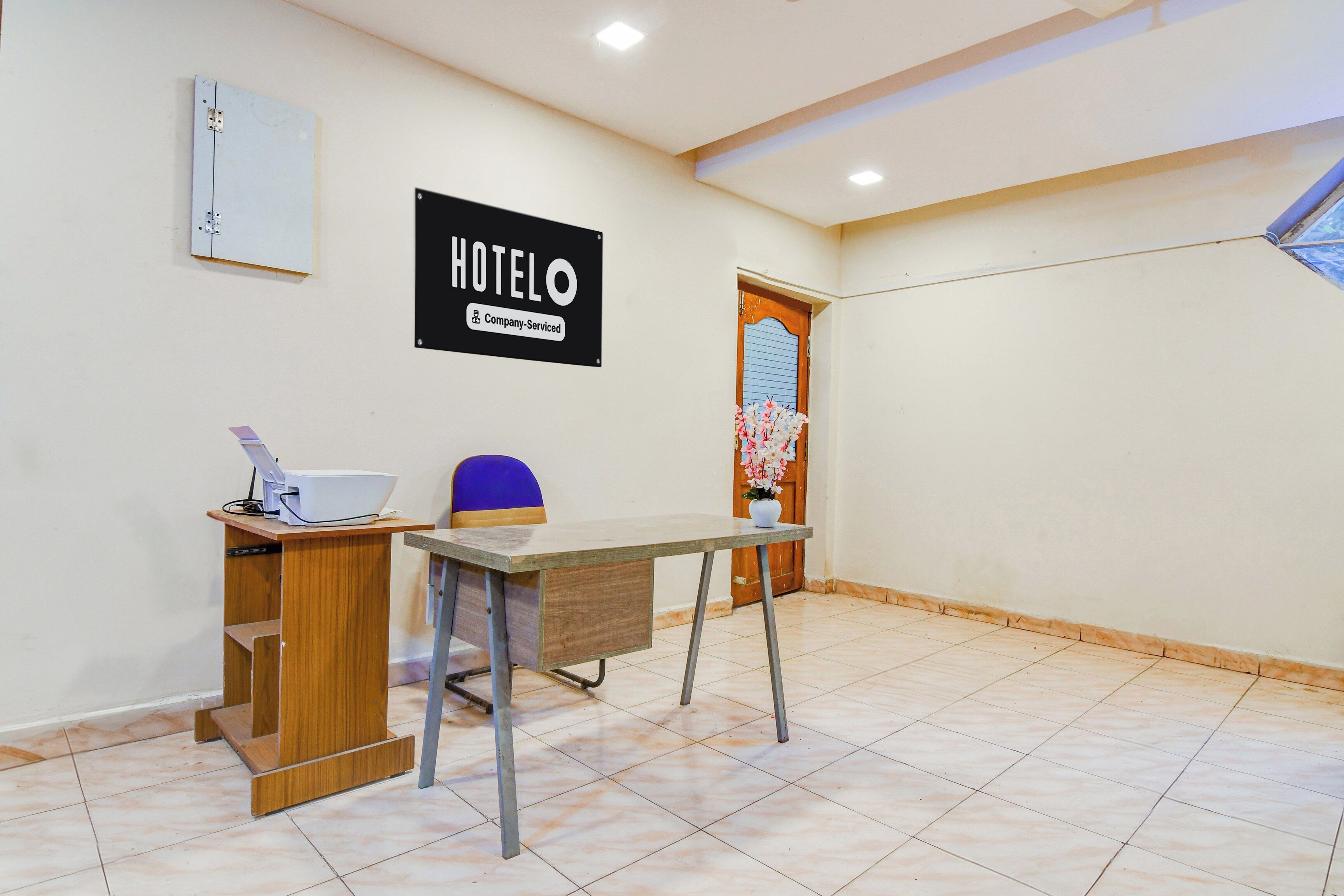 A hotel reception area with a reception desk, a chair, a wall-mounted sign, a door, and a tiled floor.
