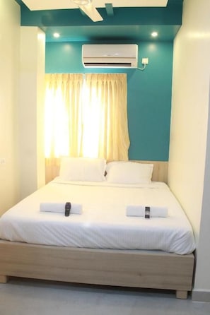 A neatly made bed with white linens and two pillows, an air conditioning unit mounted on the wall, and a window with curtains. - JFIVE RESIDENCY (Chennai)