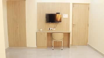 Una habitación con un armario de madera, un escritorio con silla y un televisor montado.