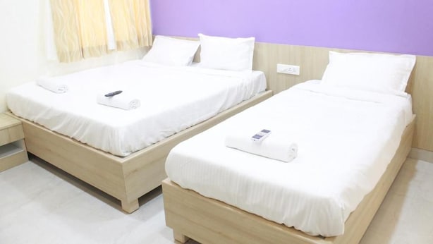 Two single beds with white bedding and a wooden headboard, a bedside table, and a wall with a purple accent. - JFIVE RESIDENCY (Chennai)