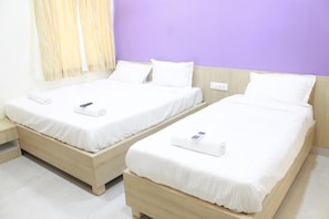 Two single beds with white bedding and a wooden headboard, a bedside table, and a wall with a purple accent. - JFIVE RESIDENCY (Chennai)