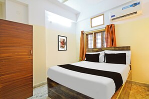 A hotel room with a bed, a wooden wardrobe, a framed picture on the wall, an air conditioning unit, and a window with curtains. - Hotel O Suncity formerly Fort Inn (Hyderabad)