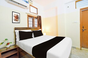 Un lit bien fait, recouvert d’une couvre-lit noire et blanche, avec une tête de lit en bois et une table de chevet sur laquelle est posée une petite plante.